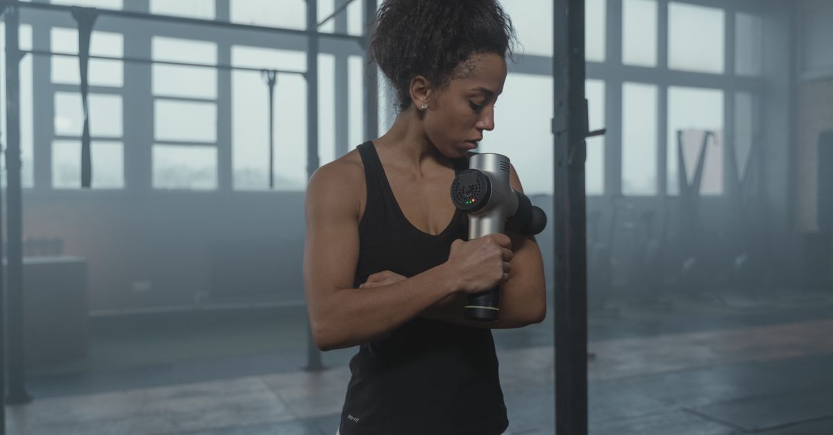 Fit woman using a massage gun in a well-lit gym studio for muscle recovery. - Evidence evidence guide for magnesium muscle soreness meta-analysis
