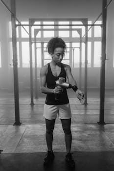 A determined woman in the gym uses a massage gun post-workout to relax.