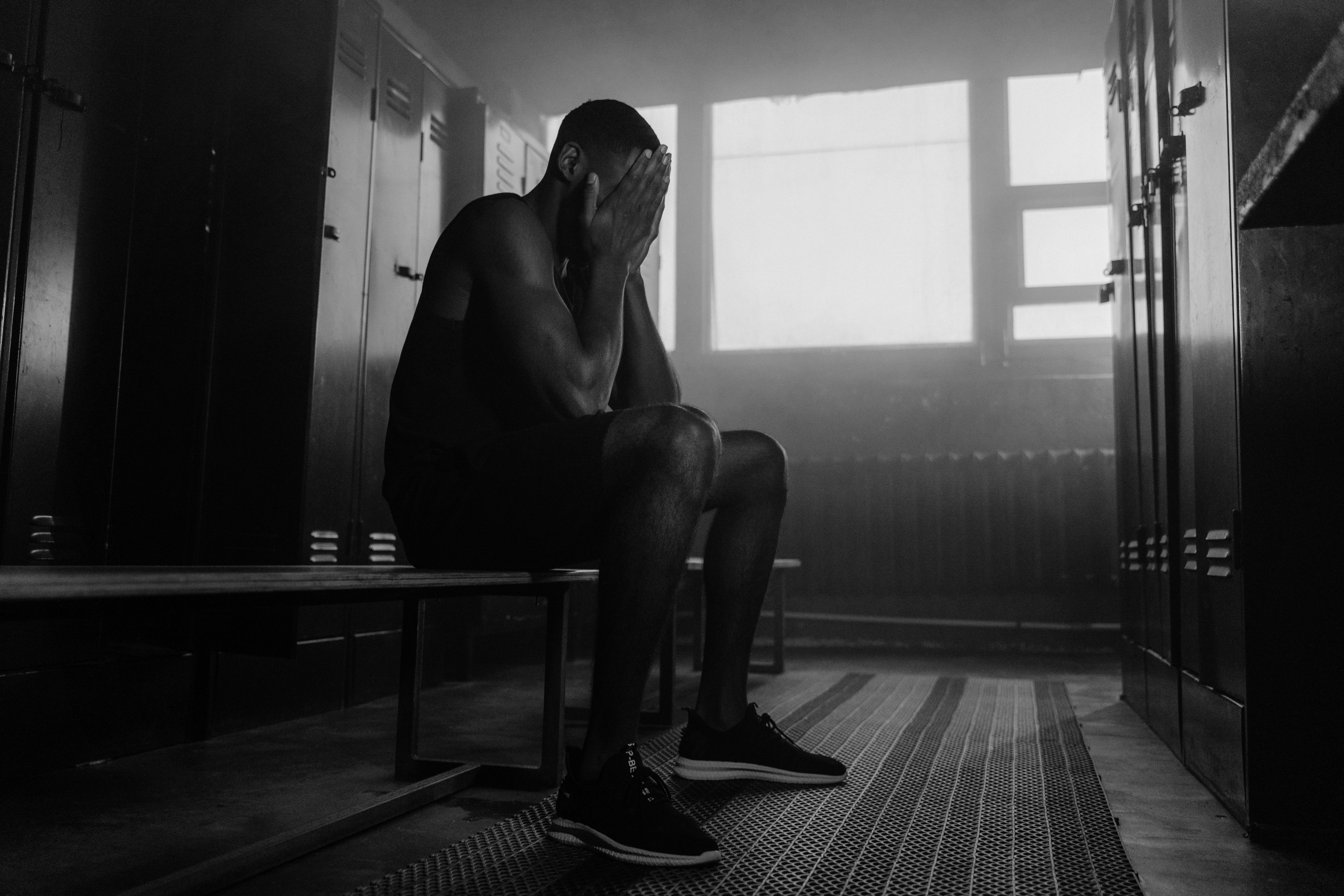 A thoughtful athlete sitting alone on a locker room bench, head in hands, out of uniform