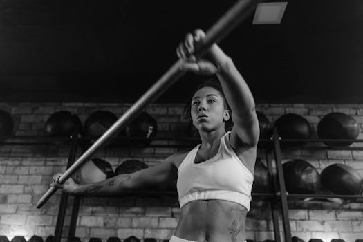 Monochrome photo of a determined woman exercising with a barbell indoors, showcasing strength.