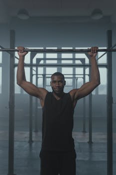 A fit African American man performing a pull-up indoors, showcasing strength and fitness.