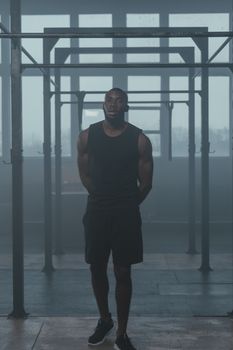 A fit man in a black tank top poses confidently in an indoor gym setting.