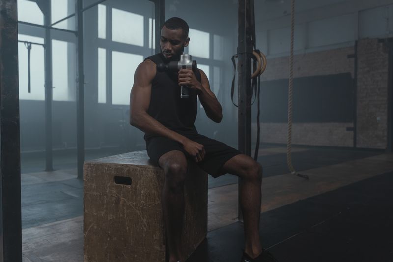 Homme utilisant un pistolet de massage sur son épaule après un entraînement sportif