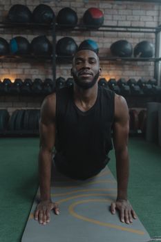 African American man doing yoga upward facing dog pose in gym for wellness.