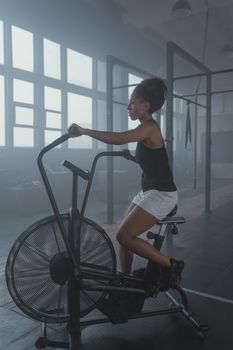 African American woman working out on an air bike in a gym, showcasing fitness and determination.