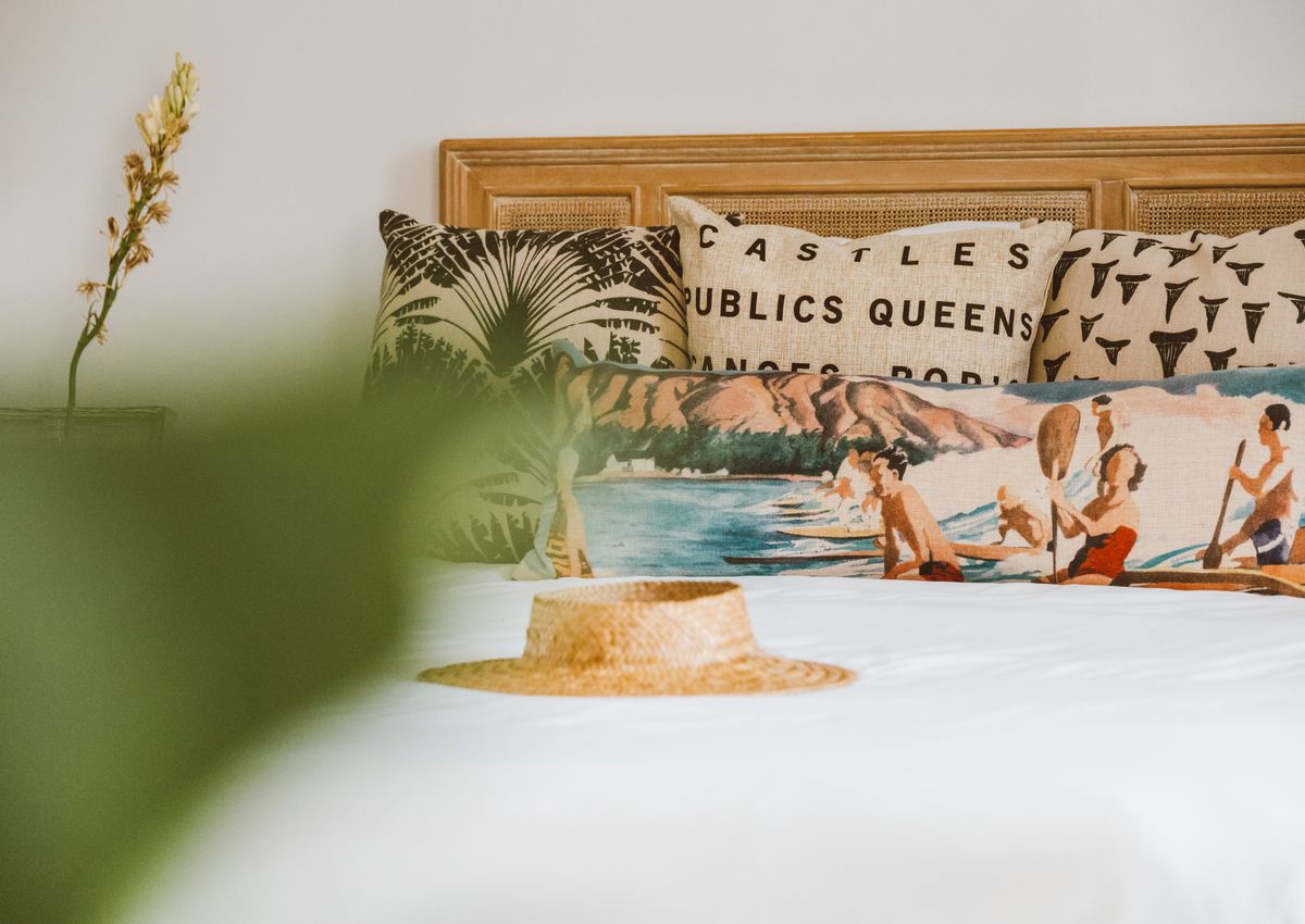 A sun hat resting on a neatly made bed with soft pillows.