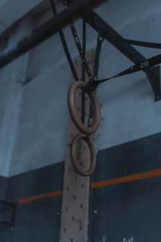 A set of wooden gymnastic rings hanging inside a dimly lit gym space.