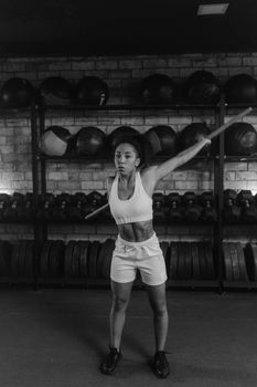 A woman in active wear exercises indoors with gym equipment in a black and white setting.