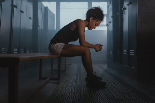 Free A contemplative athlete sits in a dimly lit locker room, embodying strength and introspection. Stock Photo