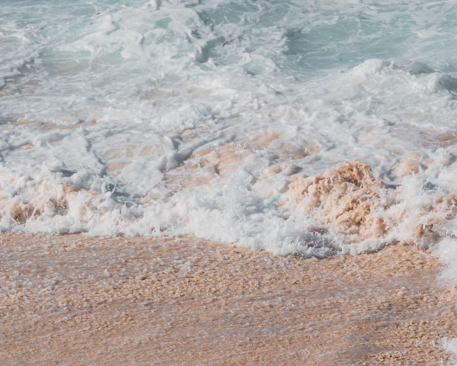 A calm ocean wave gently crashes onto a sandy beach shore, showcasing nature's tranquility.