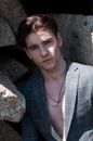 Stylish masculine model between rocks in sunlight