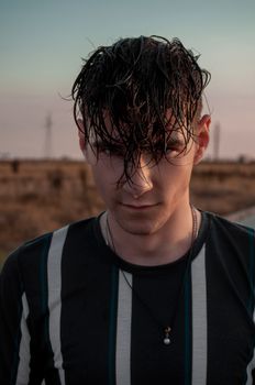 Young cool male in casual clothes with striped ornament looking at camera on road at sundown