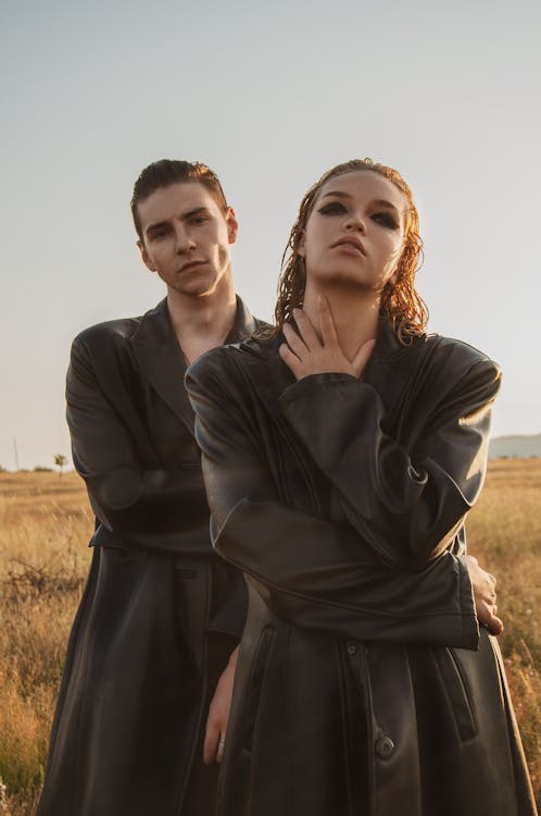 Stylish couple in similar leather cloaks in field