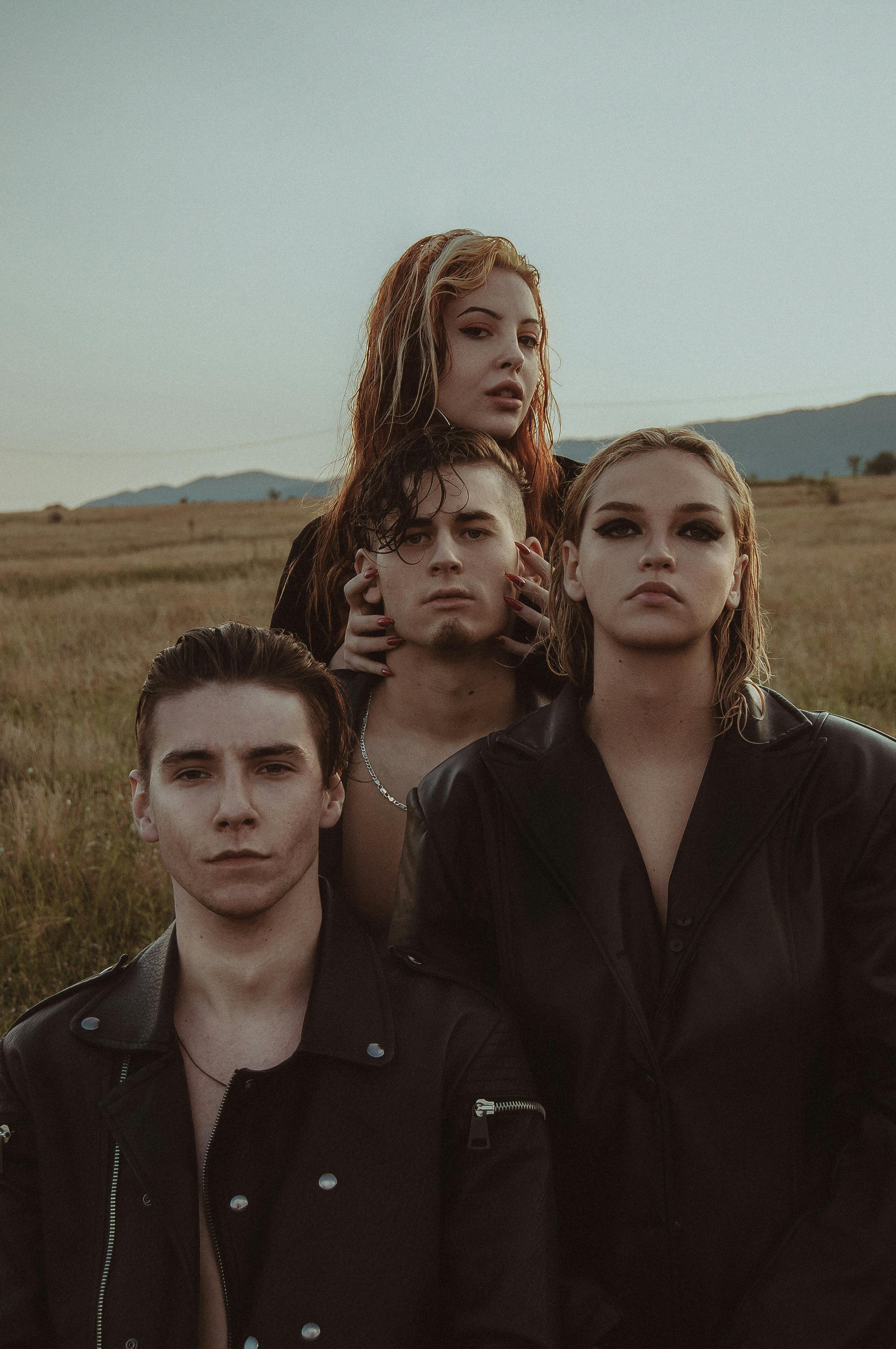 Eccentric couples wearing black clothes standing closely in rural landscape and looking at camera