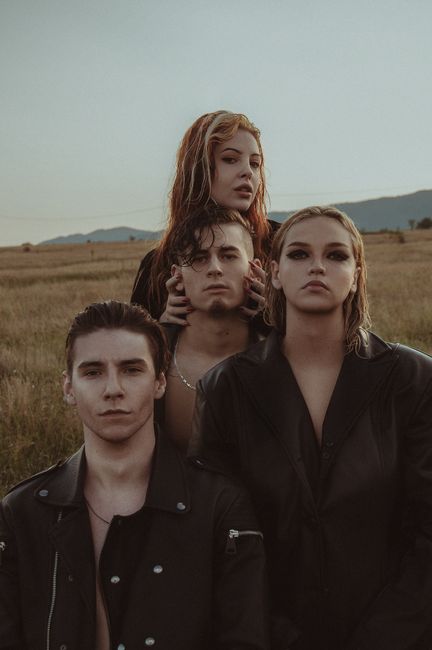 Eccentric couples wearing black clothes standing closely in rural landscape and looking at camera