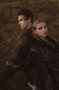 High angle of eccentric couple in stylish outfits standing back to back in grassy meadow