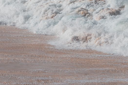 Close-up of ocean waves crashing onto sandy beach with foamy textures.
