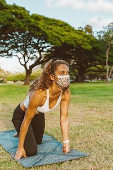 Young woman performing yoga on a mat outdoors in a sunny park.