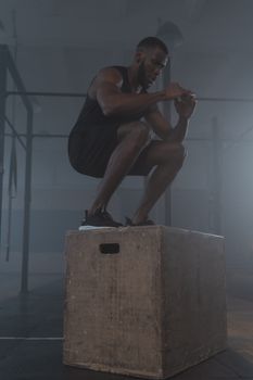 A muscular man exercising outdoors by performing squats on a wooden box for strength training.