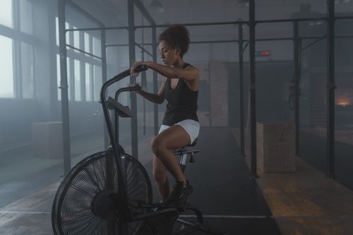 Free African American woman exercising on an air bike in a gym, showcasing fitness and strength. Stock Photo
