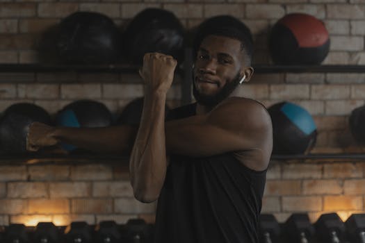 Bearded man in black tank top stretching arms in a modern gym with medicine balls background.