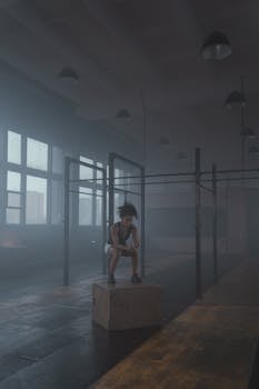 A woman focuses intensely in a dimly lit gym, surrounded by fog and workout equipment.