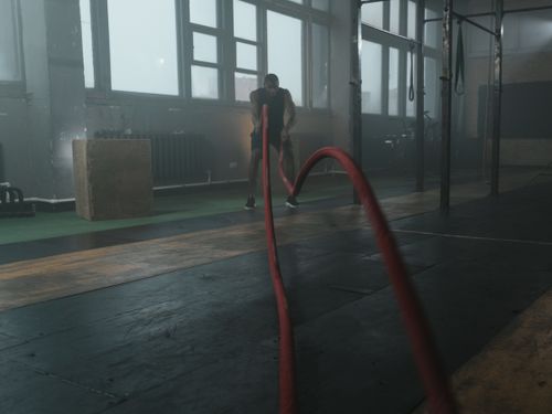 Free Man engaged in intense battle rope exercise in a gym setting, illustrating strength and endurance. Stock Photo