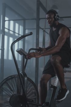 Determined man working out on exercise bike with headphones in a modern gym atmosphere.