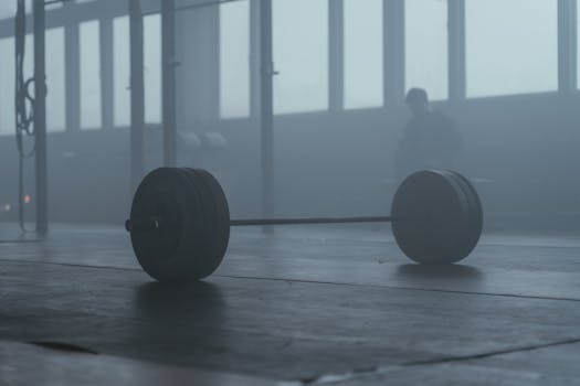 A lone barbell on the gym floor with a misty background creates a mysterious and moody ambiance.