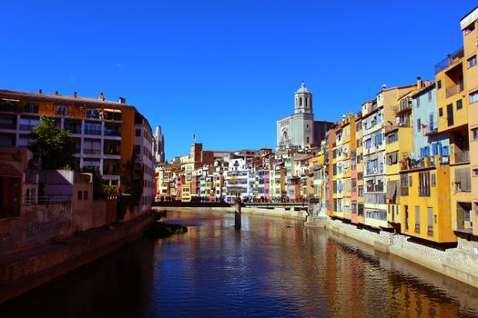 Captivating scene of Girona's iconic colorful houses along the Onyar River under a clear blue sky.