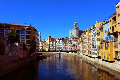 Free Captivating scene of Girona's iconic colorful houses along the Onyar River under a clear blue sky. Stock Photo
