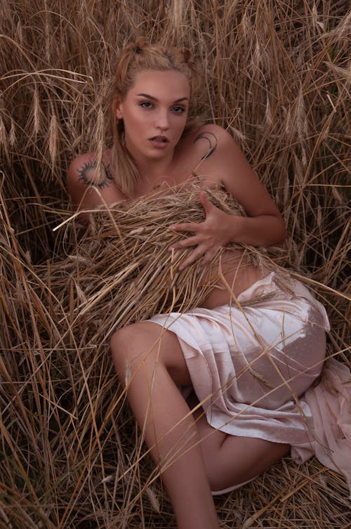 Sensual woman covering breast with dry grass in field