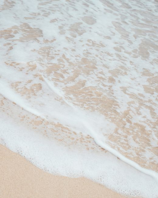 A tranquil view of gentle waves lapping on a smooth sandy beach shore.