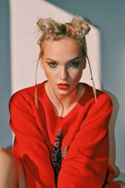 Self confident young female teen with trendy hairstyle and red lips in stylish clothes sitting on floor and looking at camera in sunlight