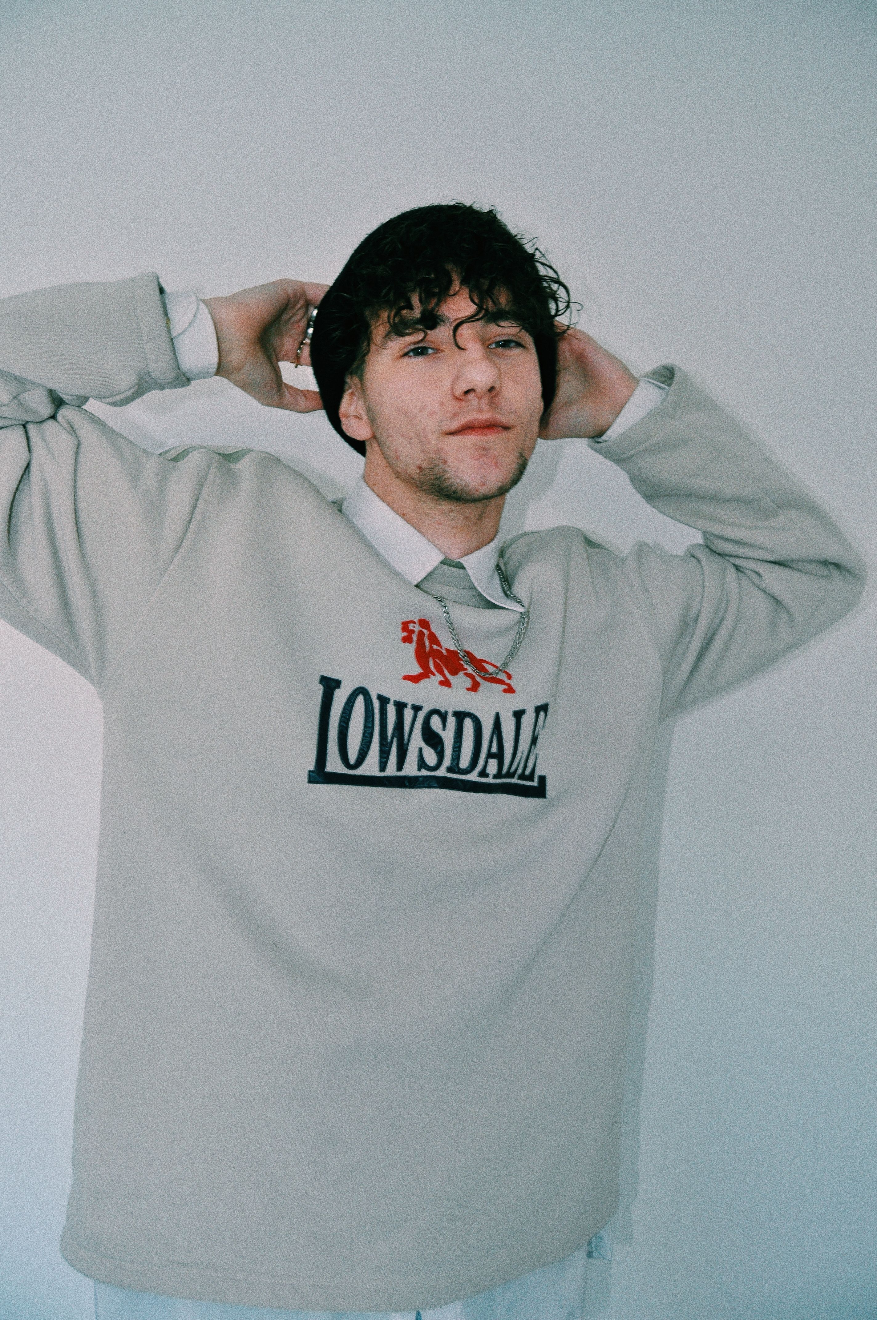 Relaxed young unshaven male millennial in stylish sweatshirt adjusting hat and looking at camera against white background