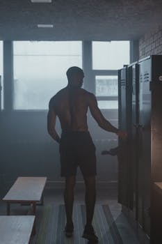 Shirtless black man standing in locker room, showcasing fit build.