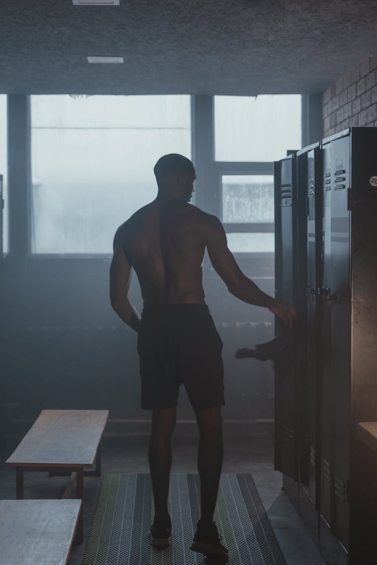 A Man In Black Shorts Standing Near The Locker At The Gym