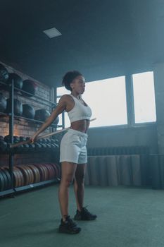 A fit young adult woman stretching indoors at the gym wearing white sportswear.