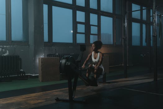 Woman working out on a rowing machine in a dimly lit industrial gym setting.