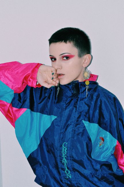 Self esteem young lady with dark short hair and makeup in trendy jacket touching face and looking at camera against white background