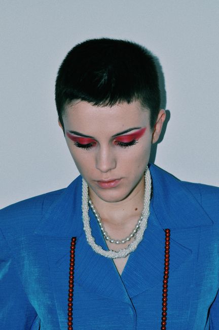 Calm young female model with dark short hair in stylish outfit and accessories demonstrating bright eyeshadow while looking down against white background
