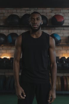 Brawny man standing in gym with blurred workout equipment. Fitness and strength focus.