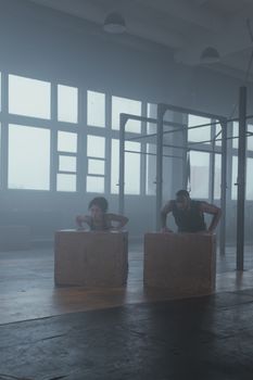 A man and woman performing push-ups on boxes during a crossfit workout inside a gym.