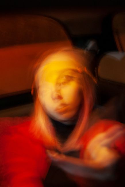 Blurred anonymous upset female teenager with blond hair sitting in dark car and looking away thoughtfully
