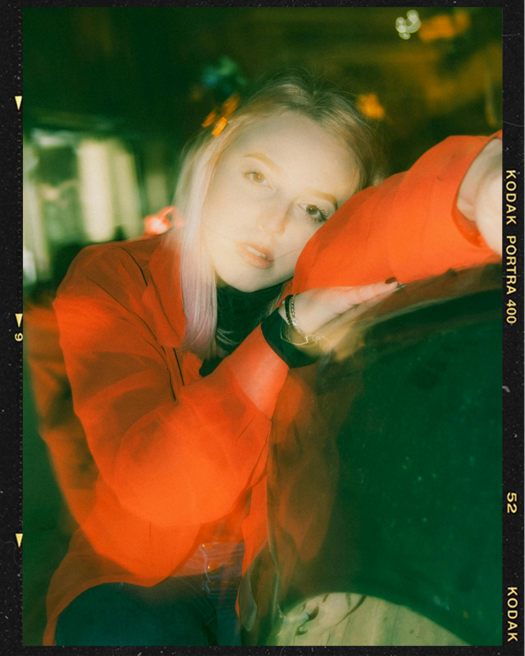 Pensive young female millennial with blond hair in casual clothes leaning head on hand and looking at camera in night city