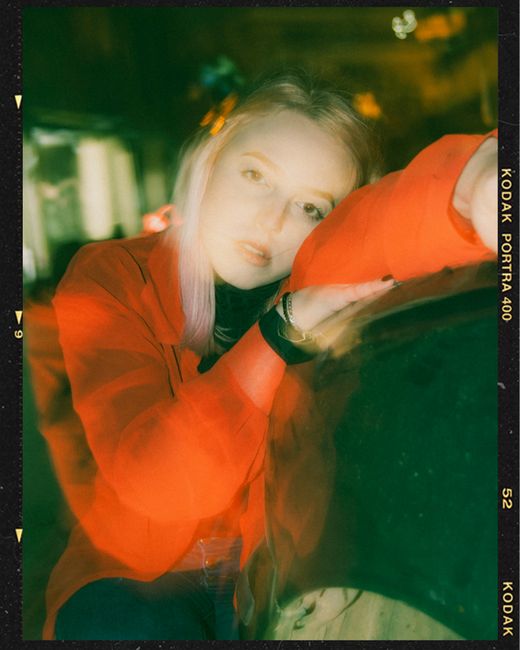 Pensive young female millennial with blond hair in casual clothes leaning head on hand and looking at camera in night city