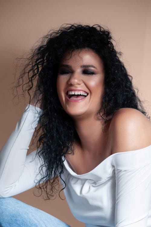 Laughing young ethnic woman with closed eyes sitting in beige studio