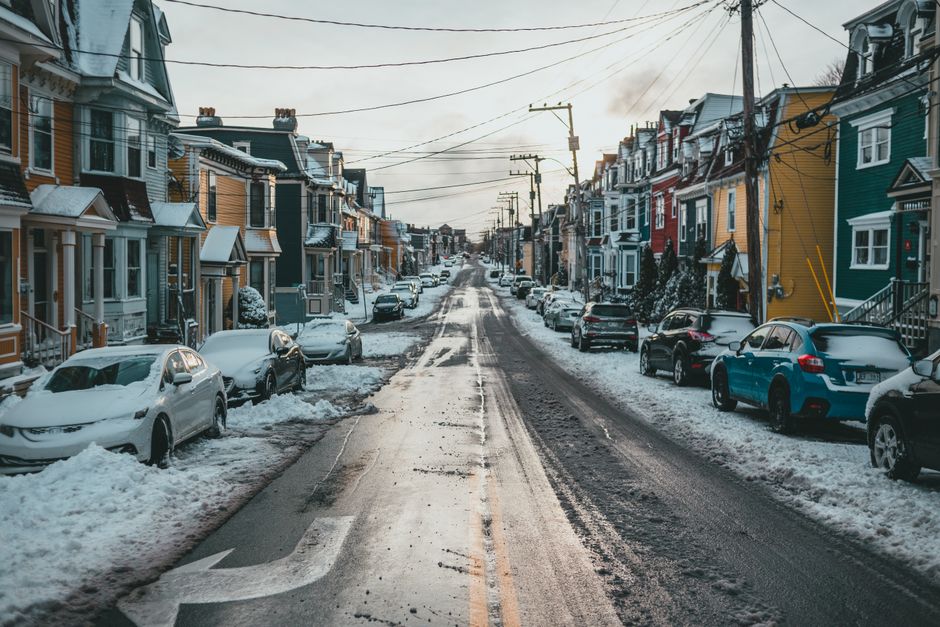 Asphalt roadway with snow and arrow between parked automobiles and dwelling building facades on winter day