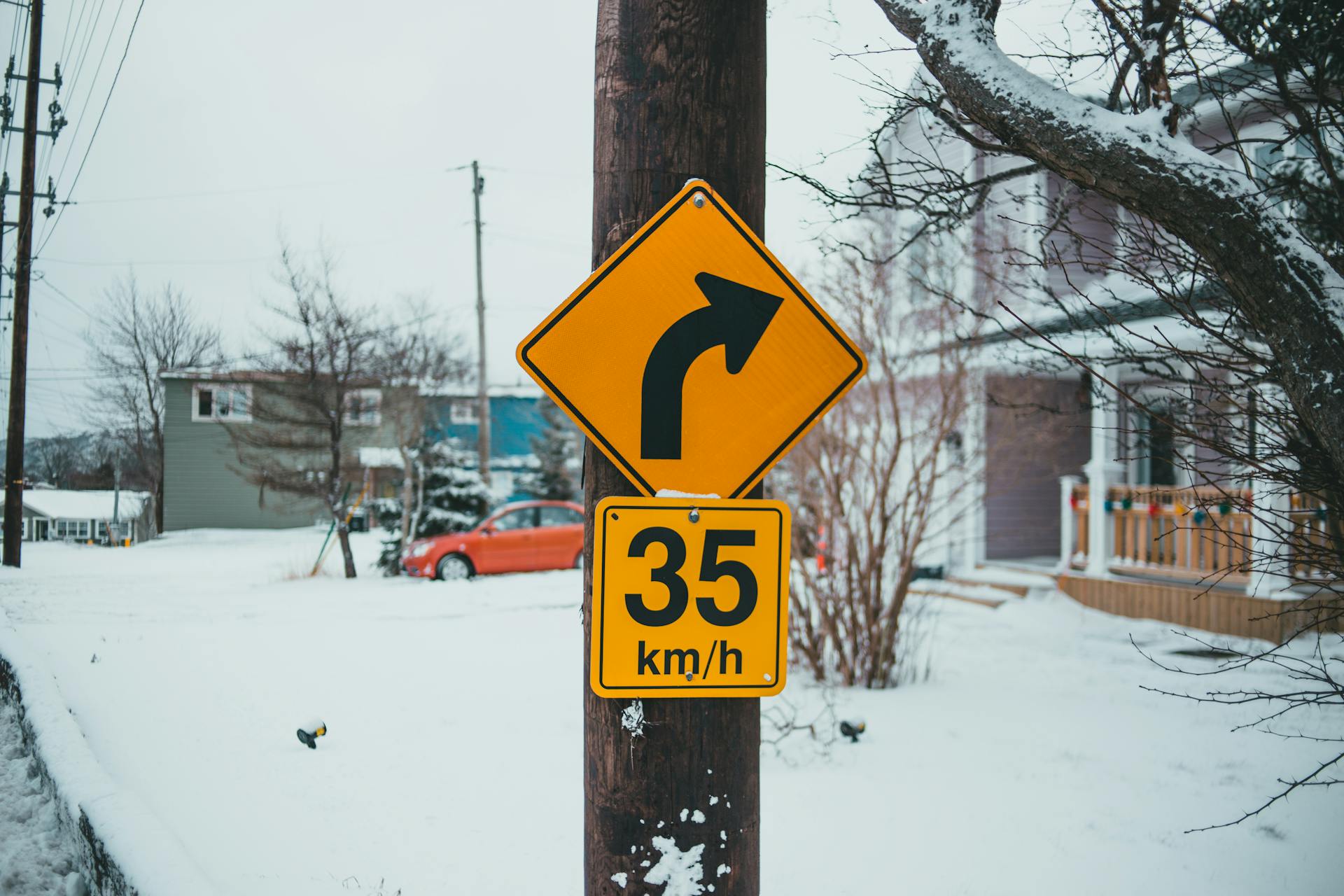 Control road signs with arrow showing turn under speed limit on post against buildings with snow in wintertime