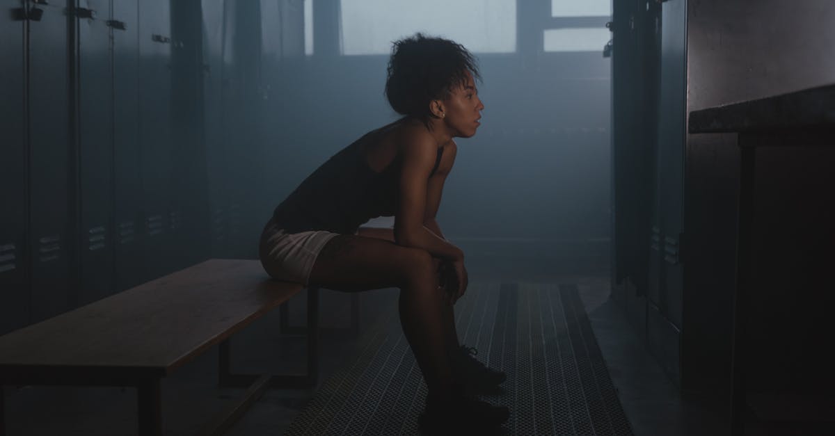 Professional athlete sitting alone in a dark locker room, head in hands, looking exhausted
